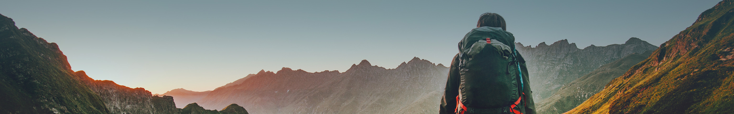 Man hiking on a mountain with large camping backpack on, with large moutains in the distance